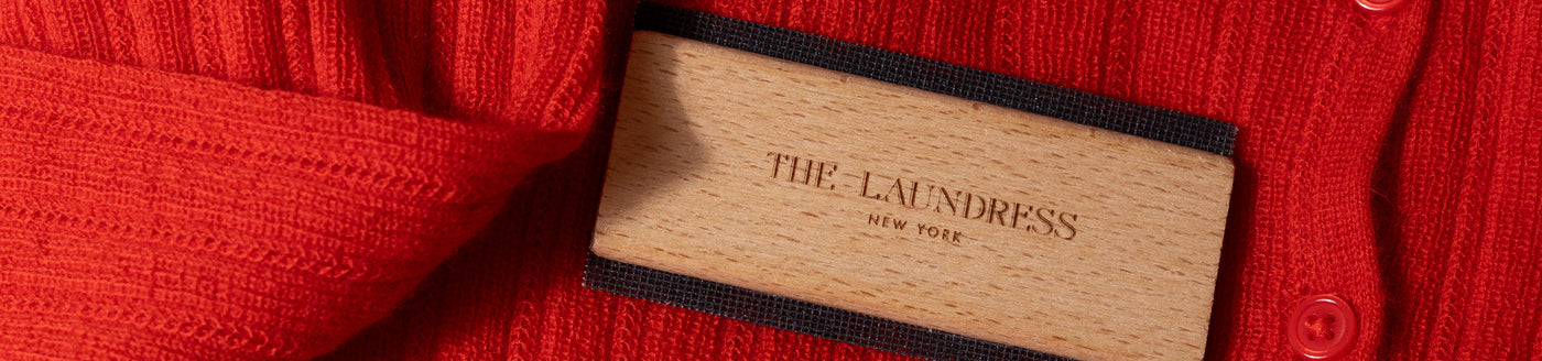 The Laundress Sweater Comb, for depilling and lifting fuzz from sweaters, sits on a red sweater. 